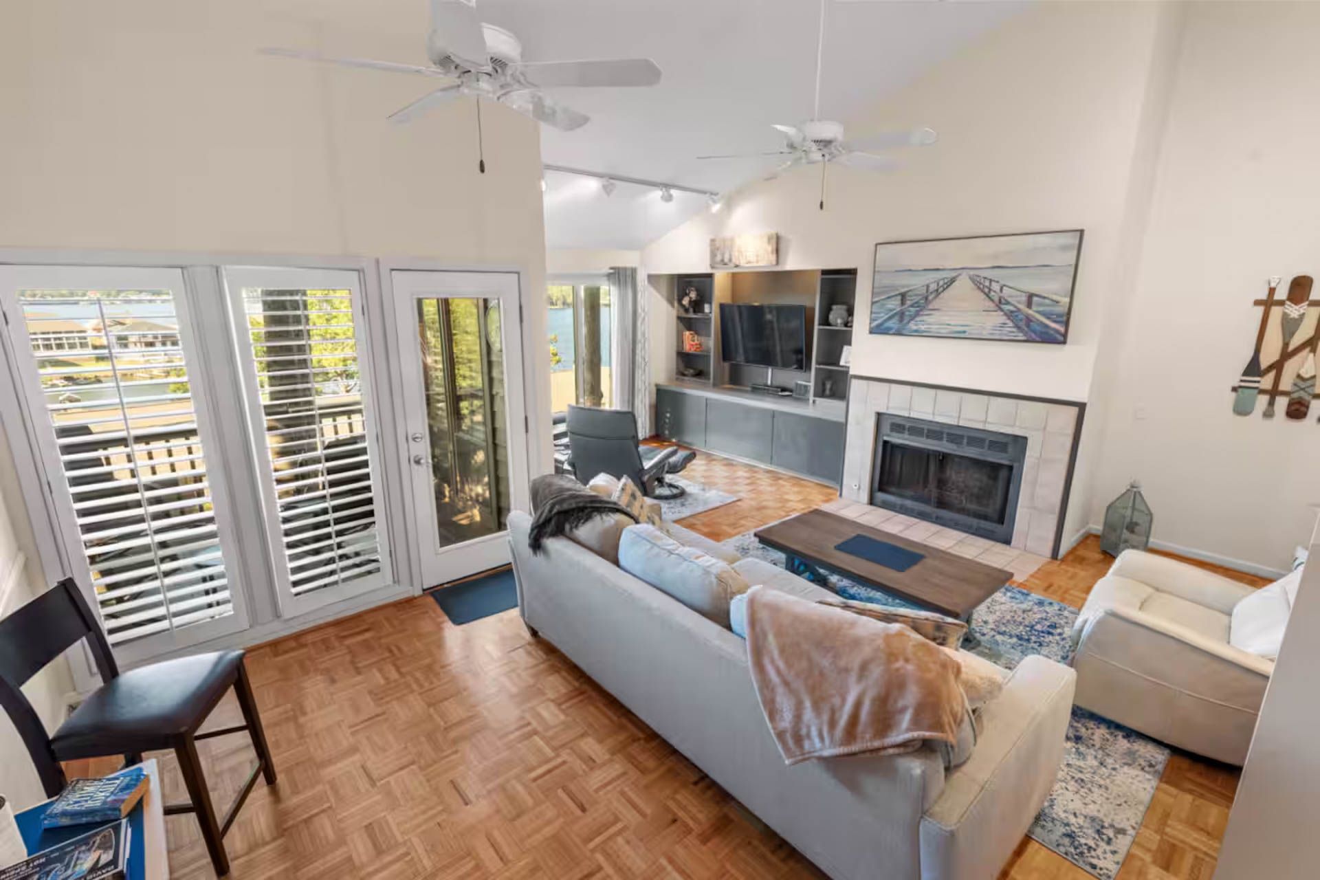 Living room with white walls, fireplace, and sofa, leading to a balcony with open shutter doors.
