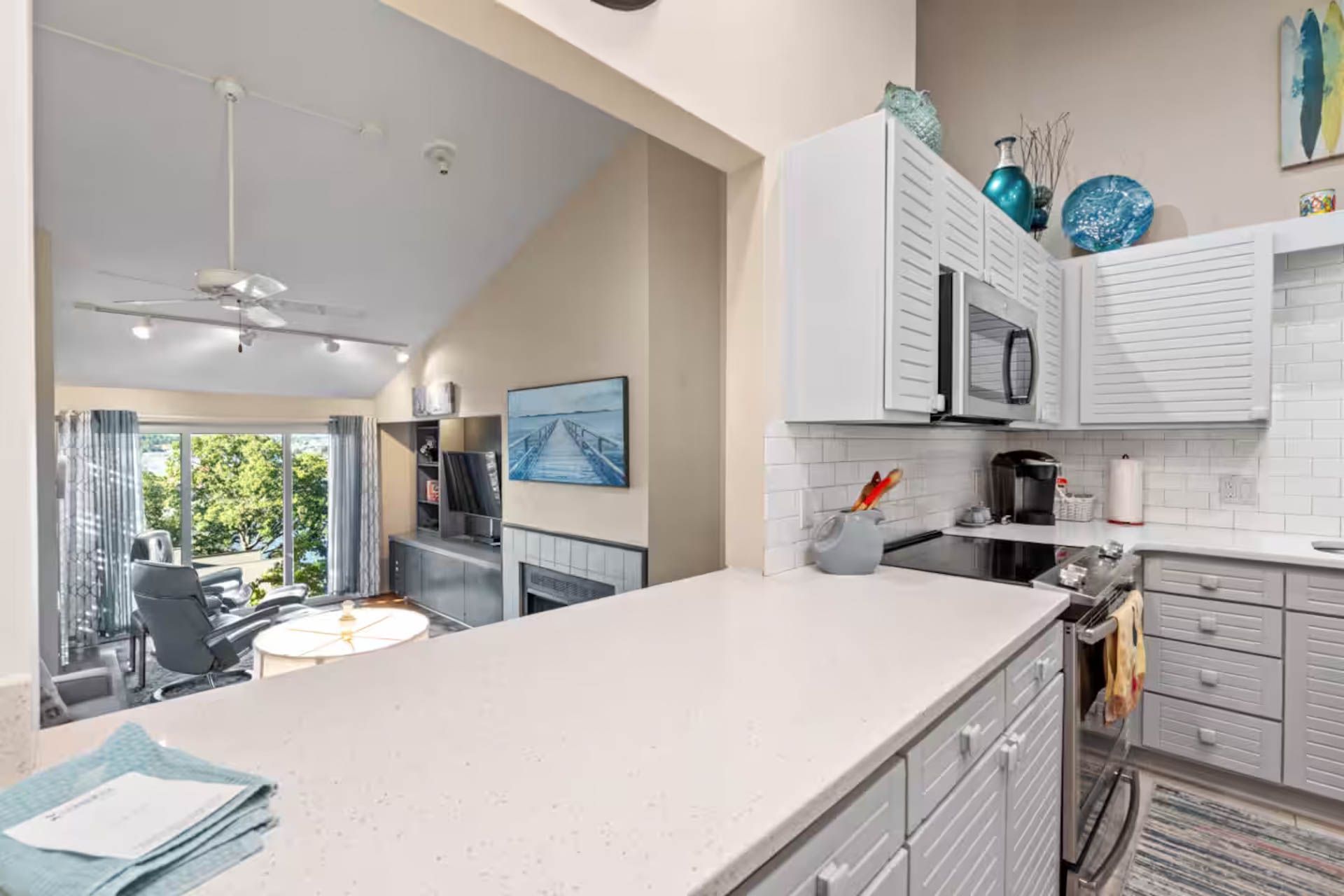 Kitchen with white cabinets, countertop, and appliances, open to a living area with a fireplace and sliding glass door.