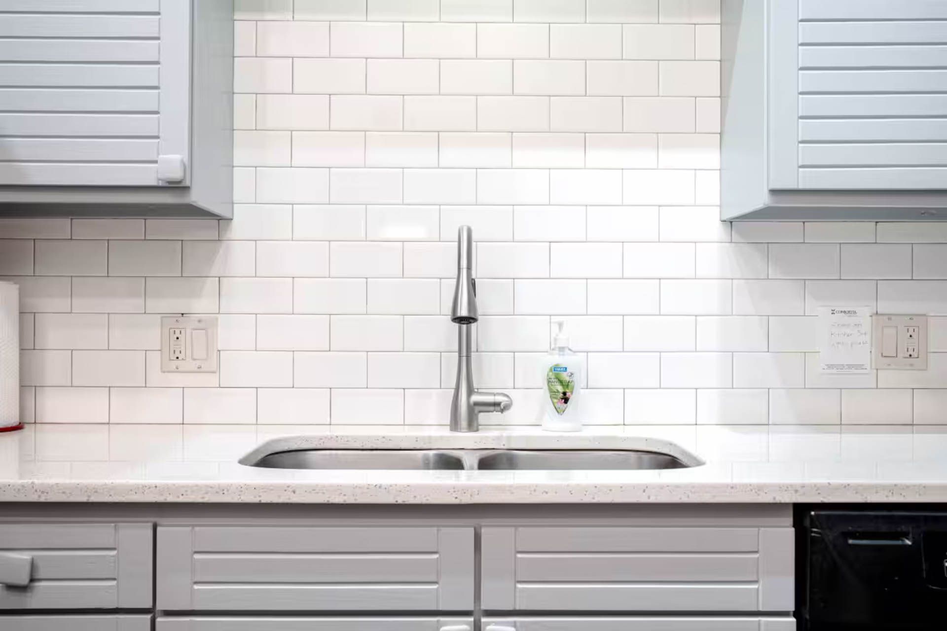 Kitchen sink with white tile backsplash, gray cabinets, and stainless steel faucet.