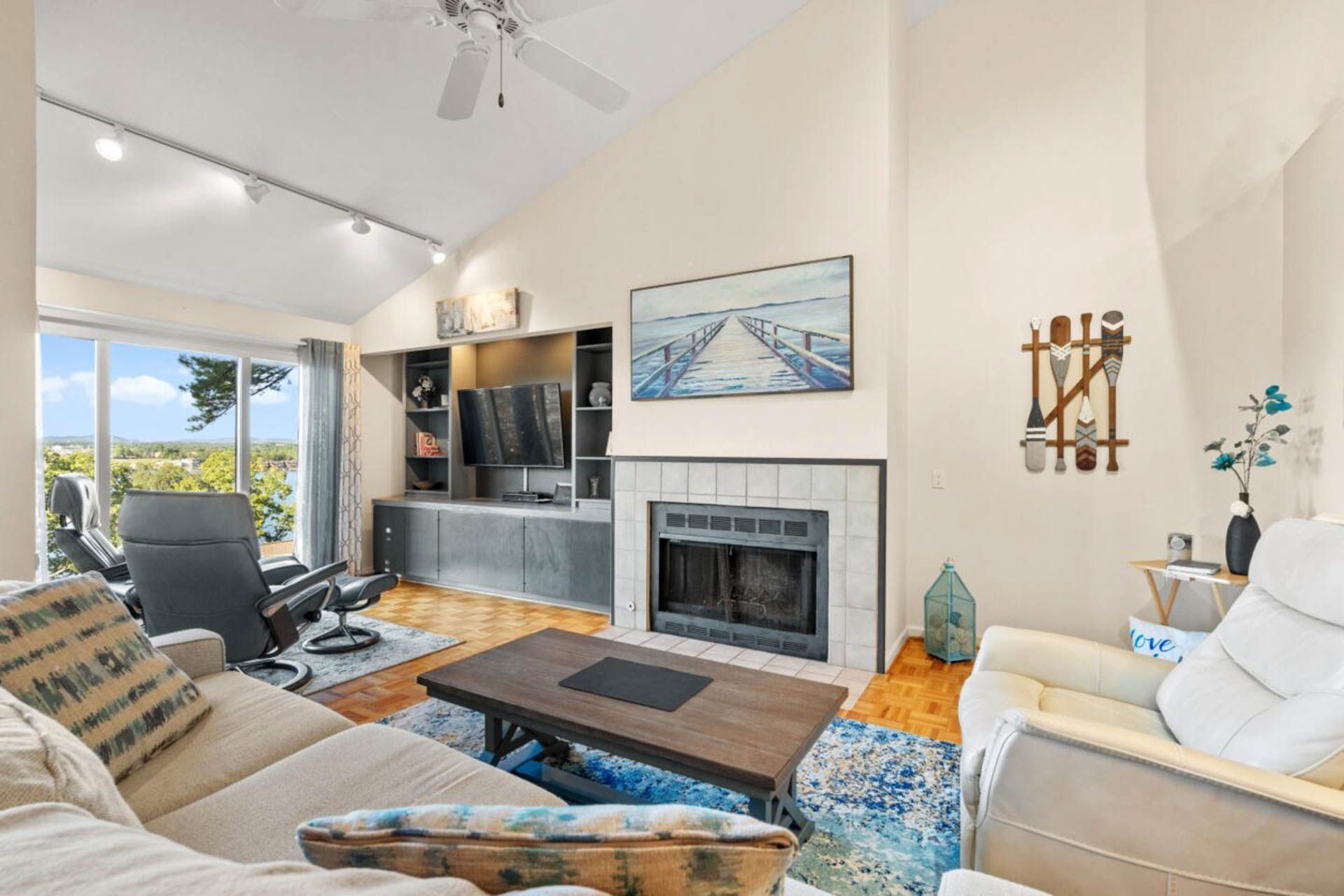 Living room with vaulted ceiling, fireplace, and view through a large window.
