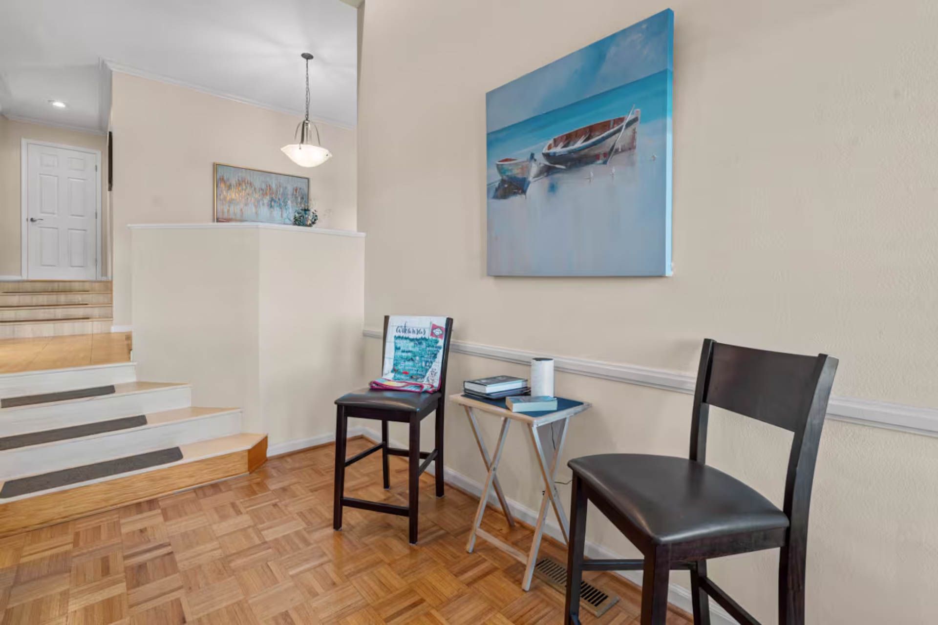 Entryway with wooden floors, staircase, two chairs, and a painting of a boat.