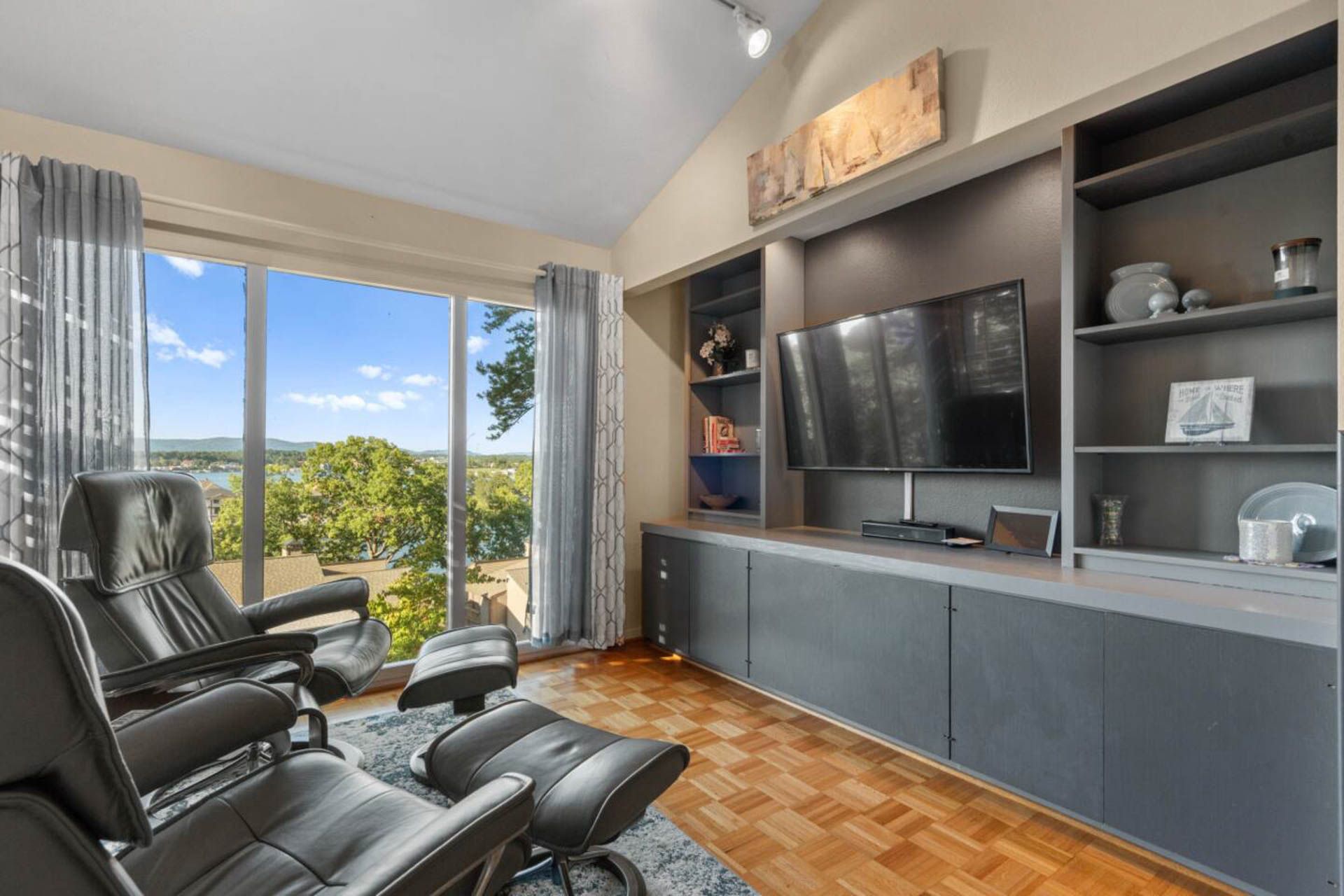 Living room with two recliners facing a large window, entertainment center, and a cityscape view.