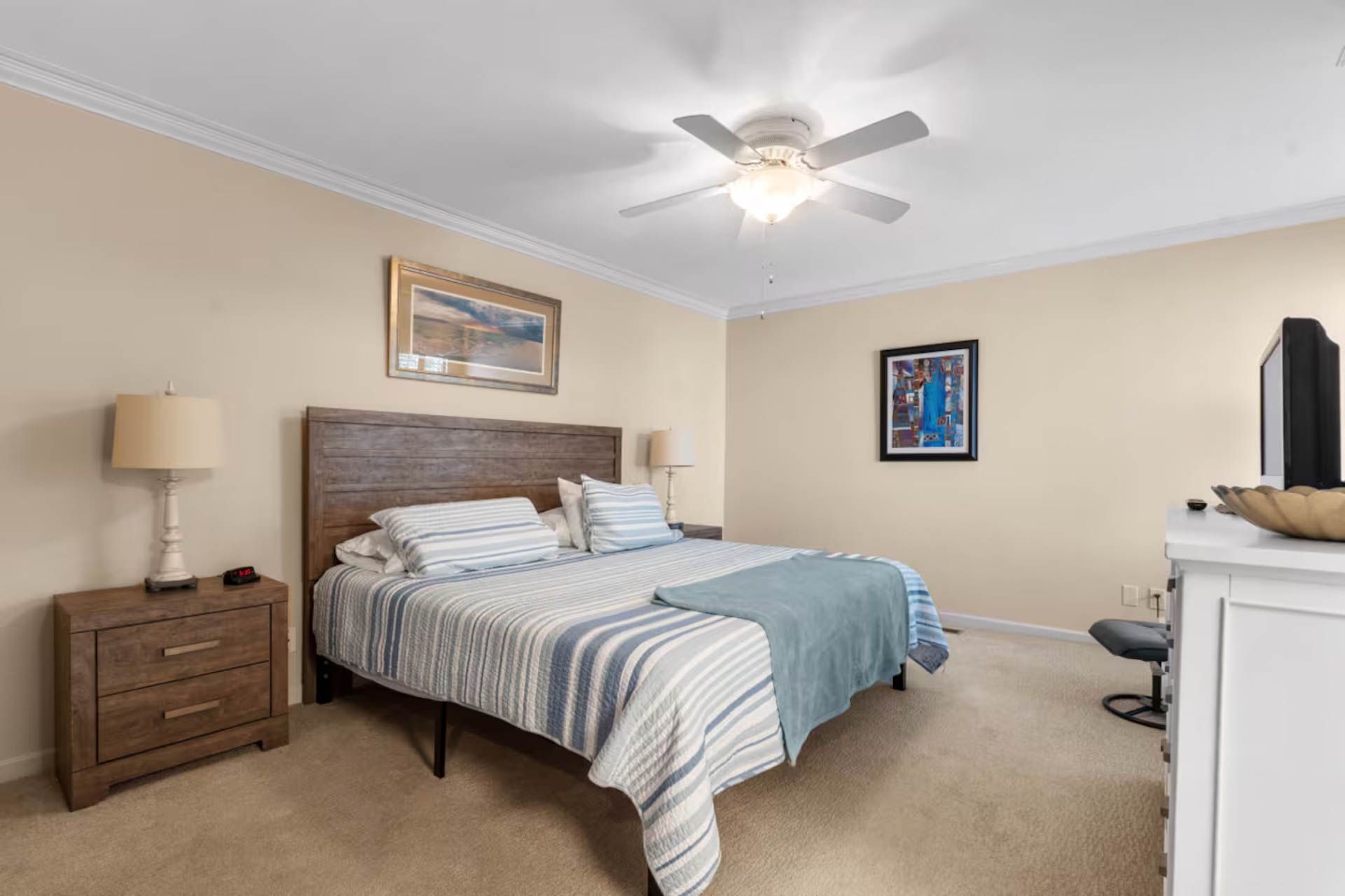Bedroom with a bed, nightstand, and dresser. Light beige walls, blue and white bedding, and a ceiling fan.