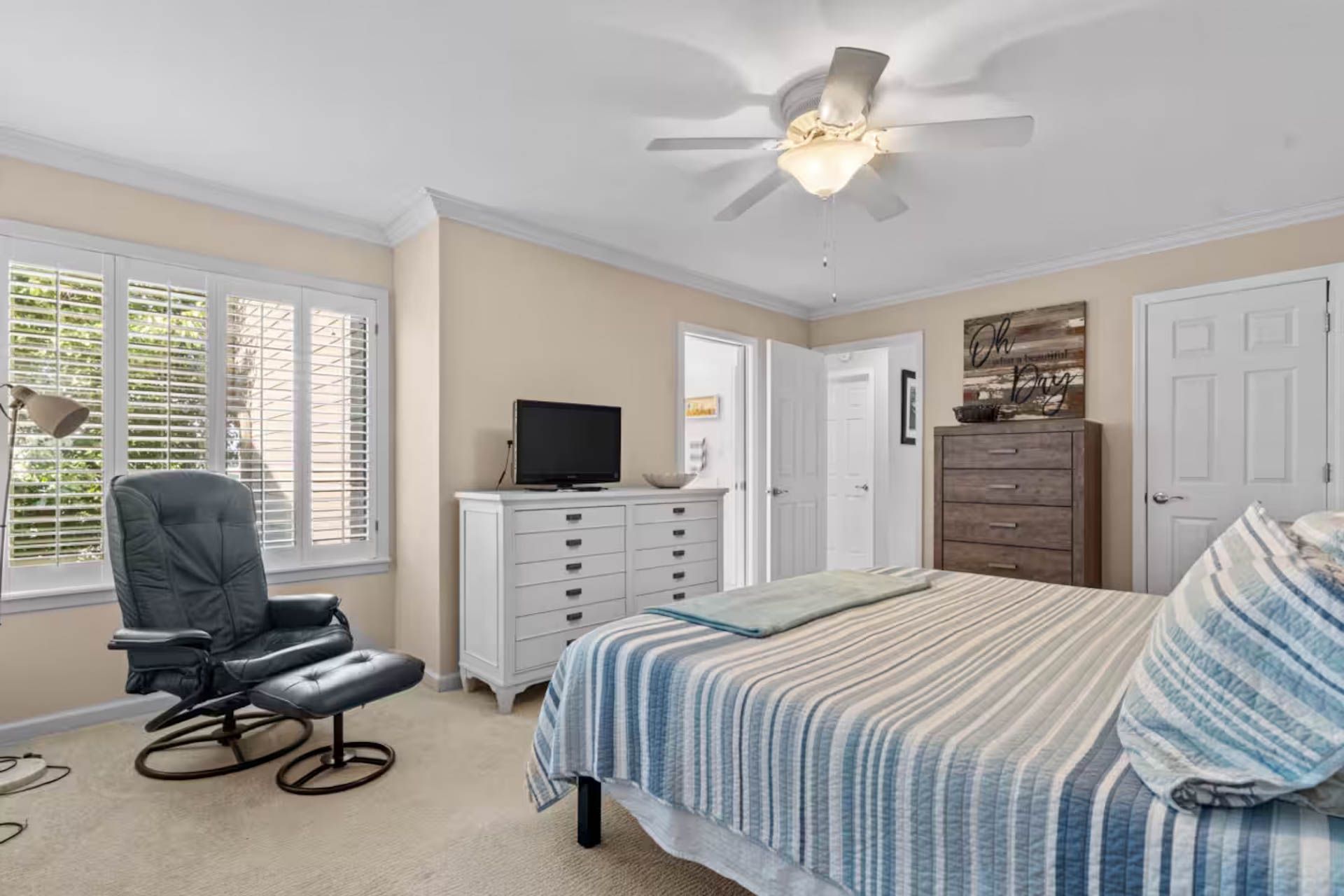 Bedroom with bed, chair, and dresser. Window with shutters. Ceiling fan.