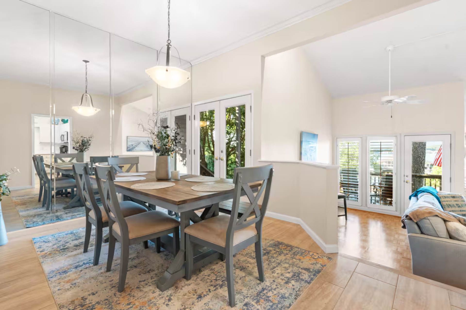 Dining room with wooden table, chairs, mirror, rug, and access to a living area and balcony.