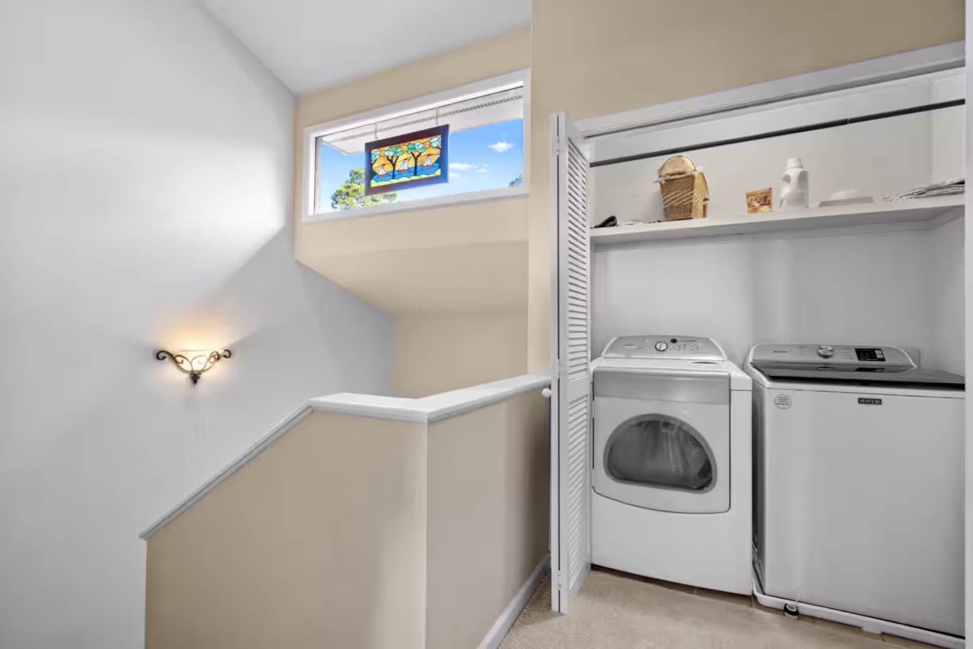 Laundry room with washer, dryer, closet, and window overlooking a sunny sky.