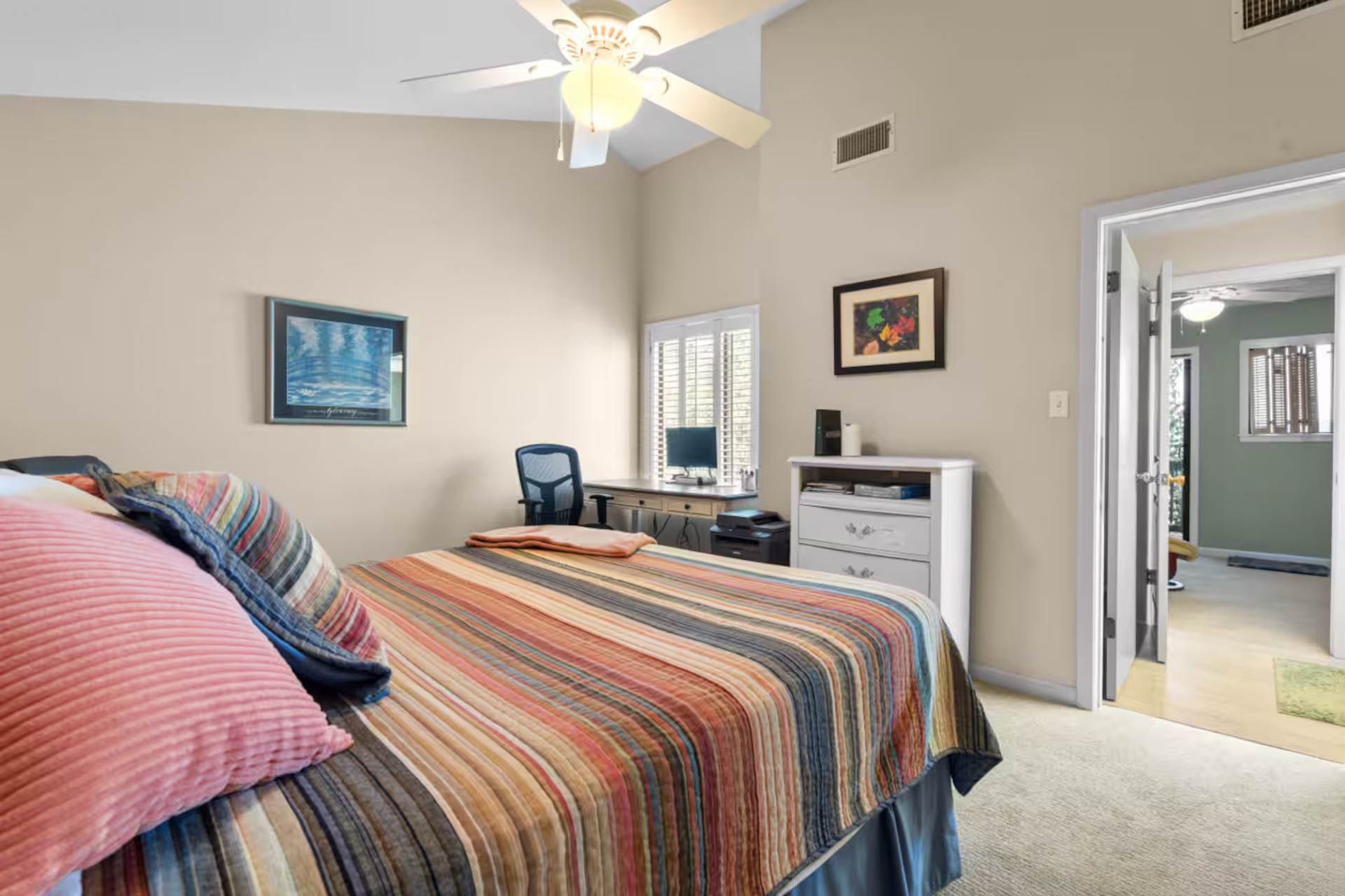 Bedroom with bed, desk, and doorway to another room; neutral colors.