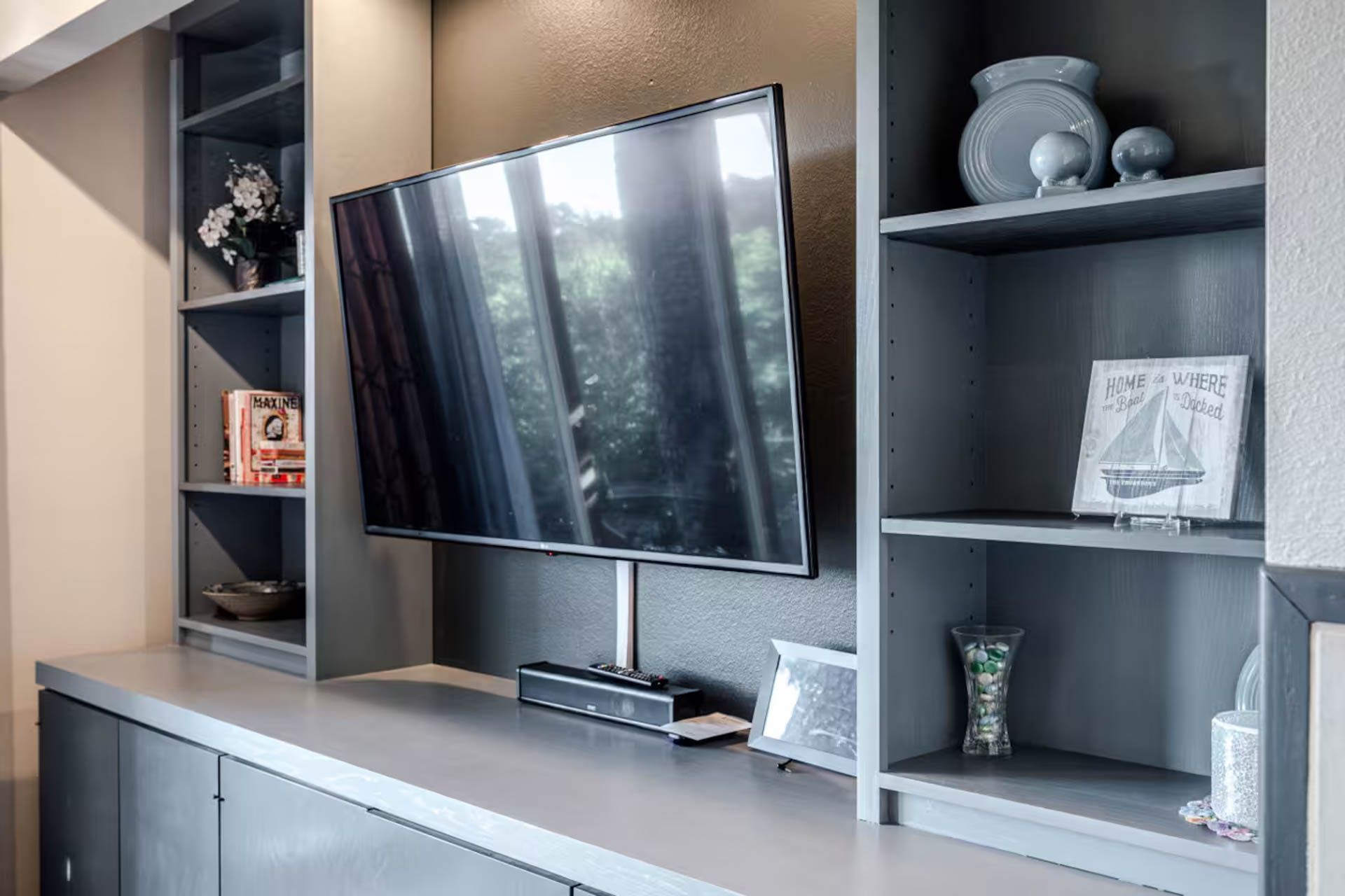 Gray built-in entertainment center with mounted TV, bookshelves, and decorative items.
