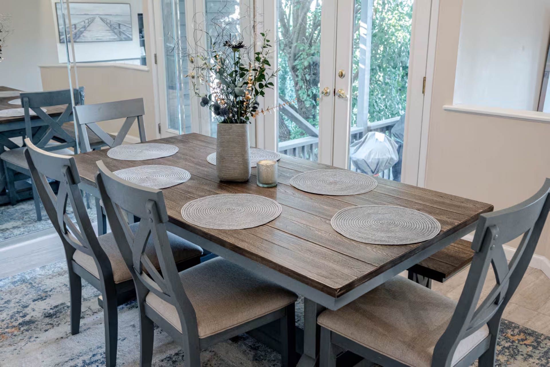 Dining table set for four near french doors; light wood and gray chairs.