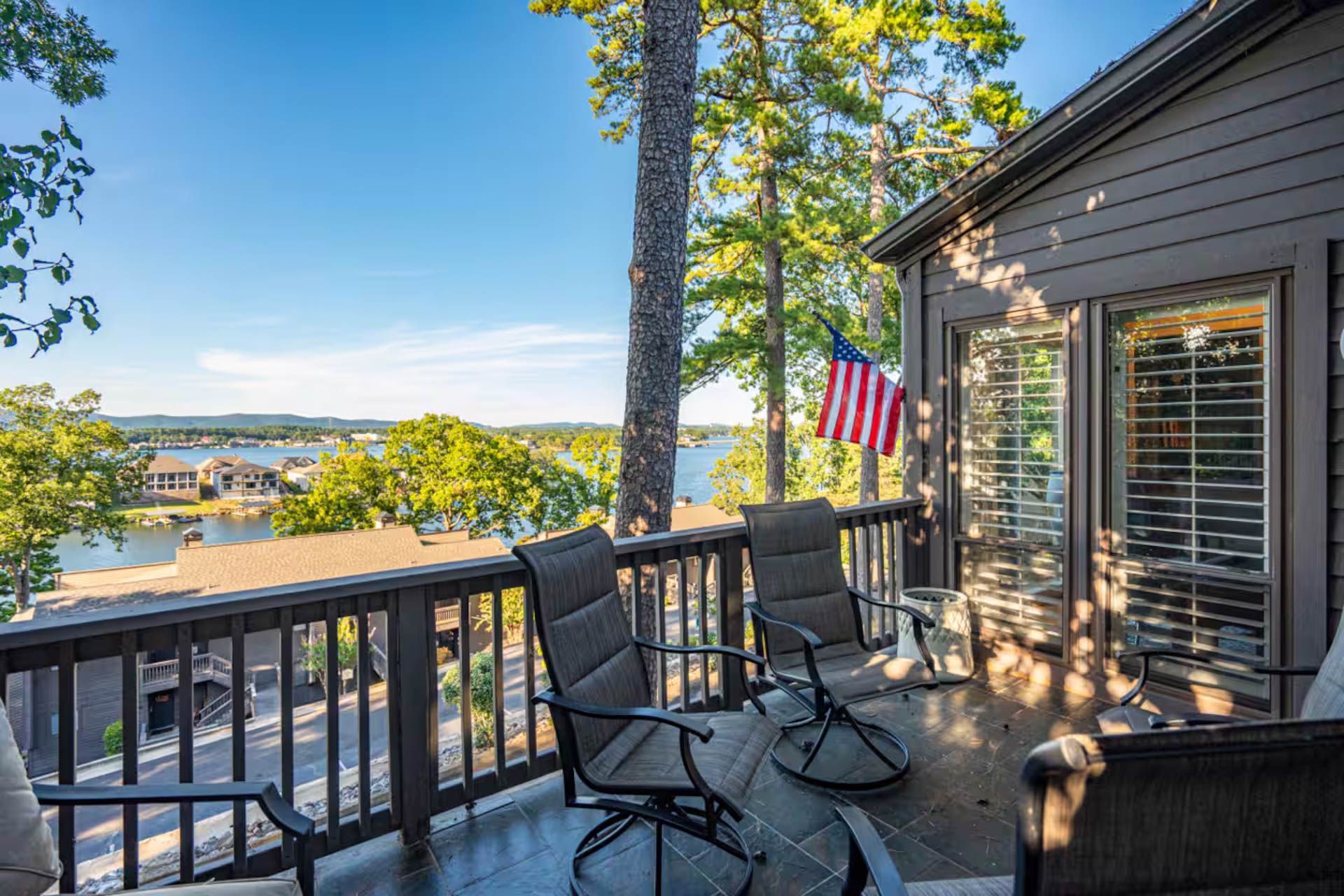 Deck overlooking a lake; two chairs face water, American flag hangs from the house.