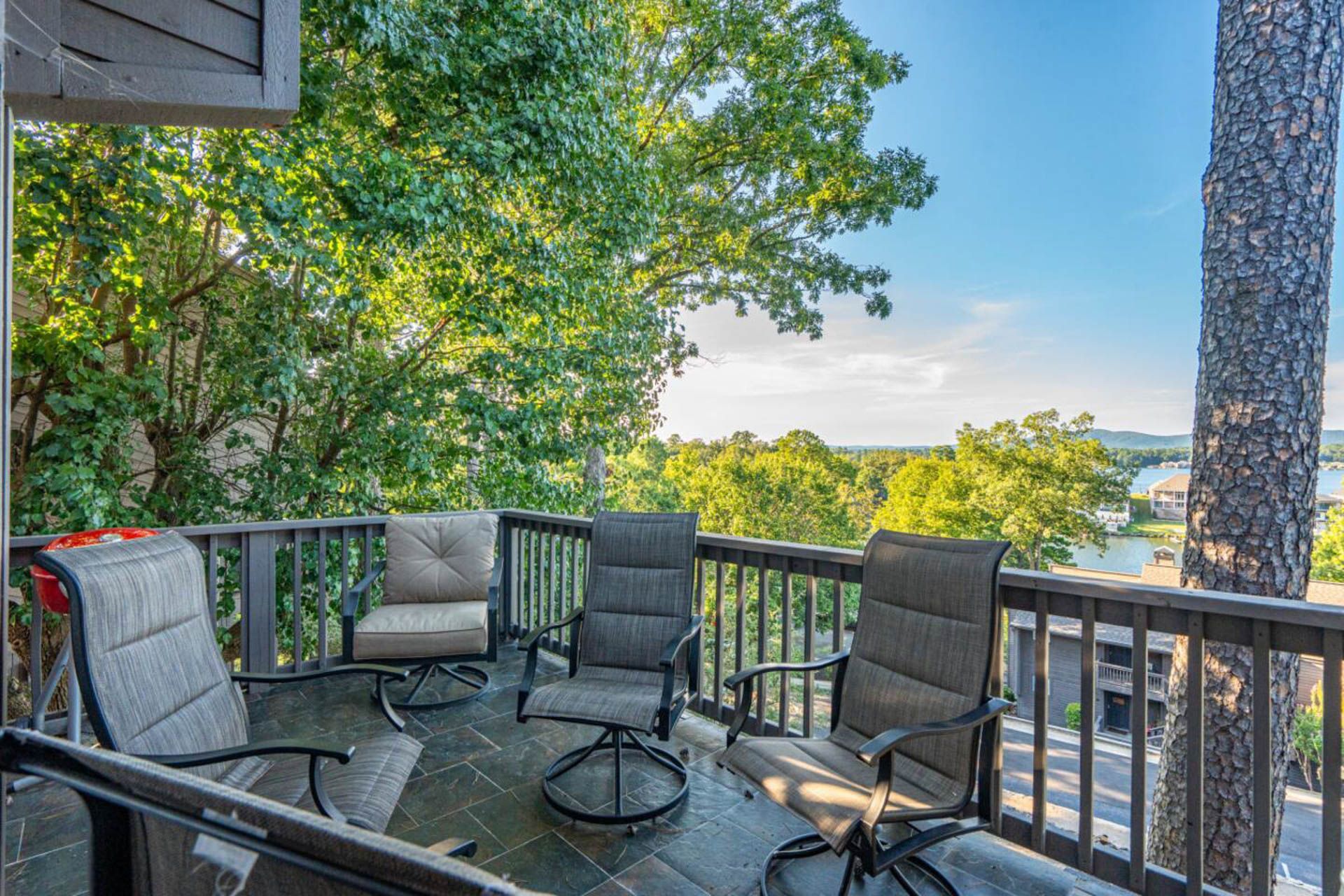 Patio with seating overlooking trees and water under a blue sky.