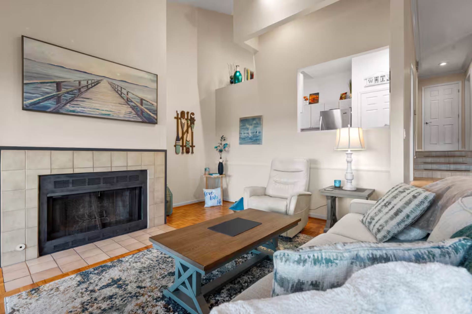 Living room with fireplace, sofa, and wood floor. Painting over the fireplace. Light colors.