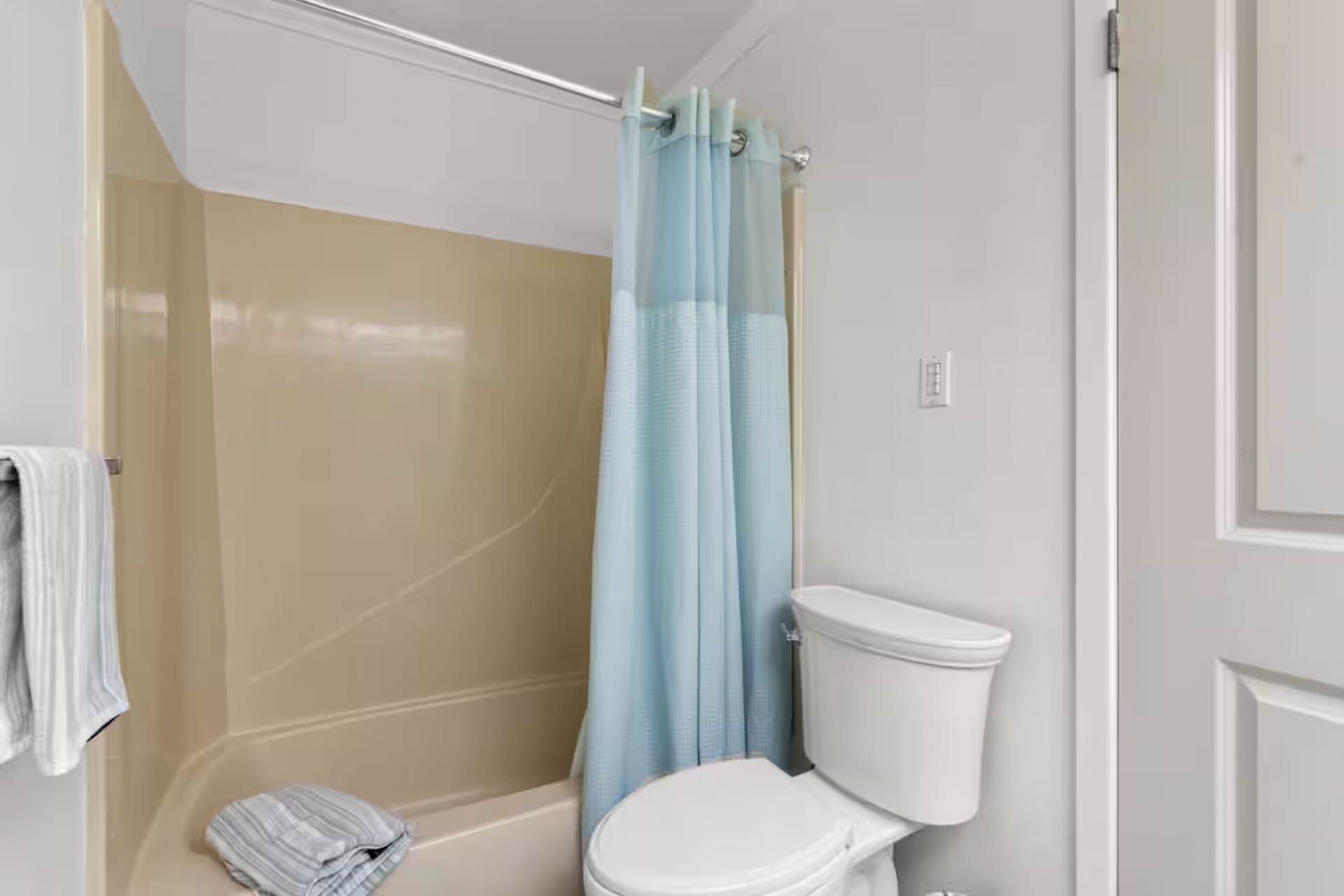 Bathroom with beige shower/tub, blue shower curtain, white toilet, and white door.