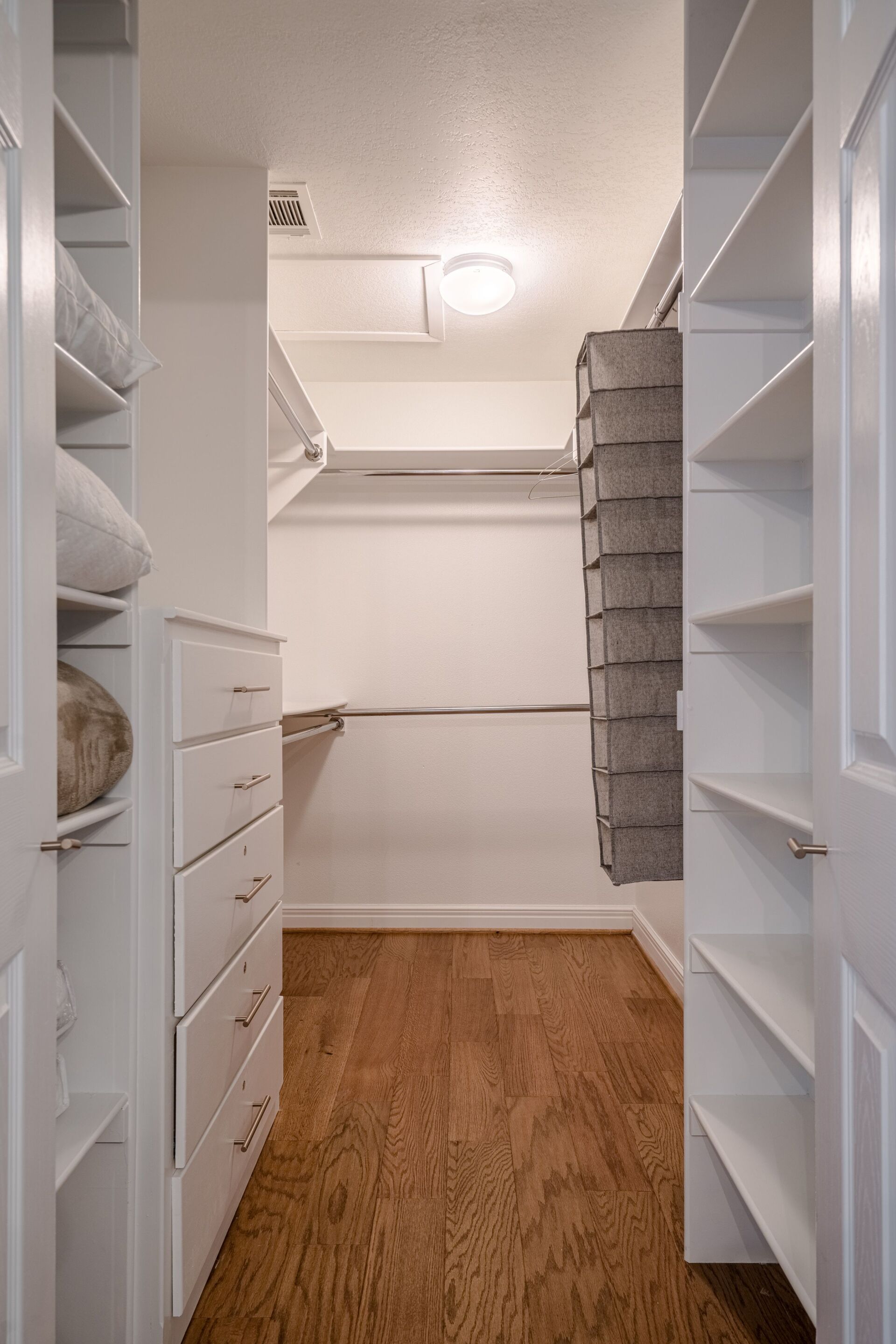A walk in closet with hardwood floors and white shelves.