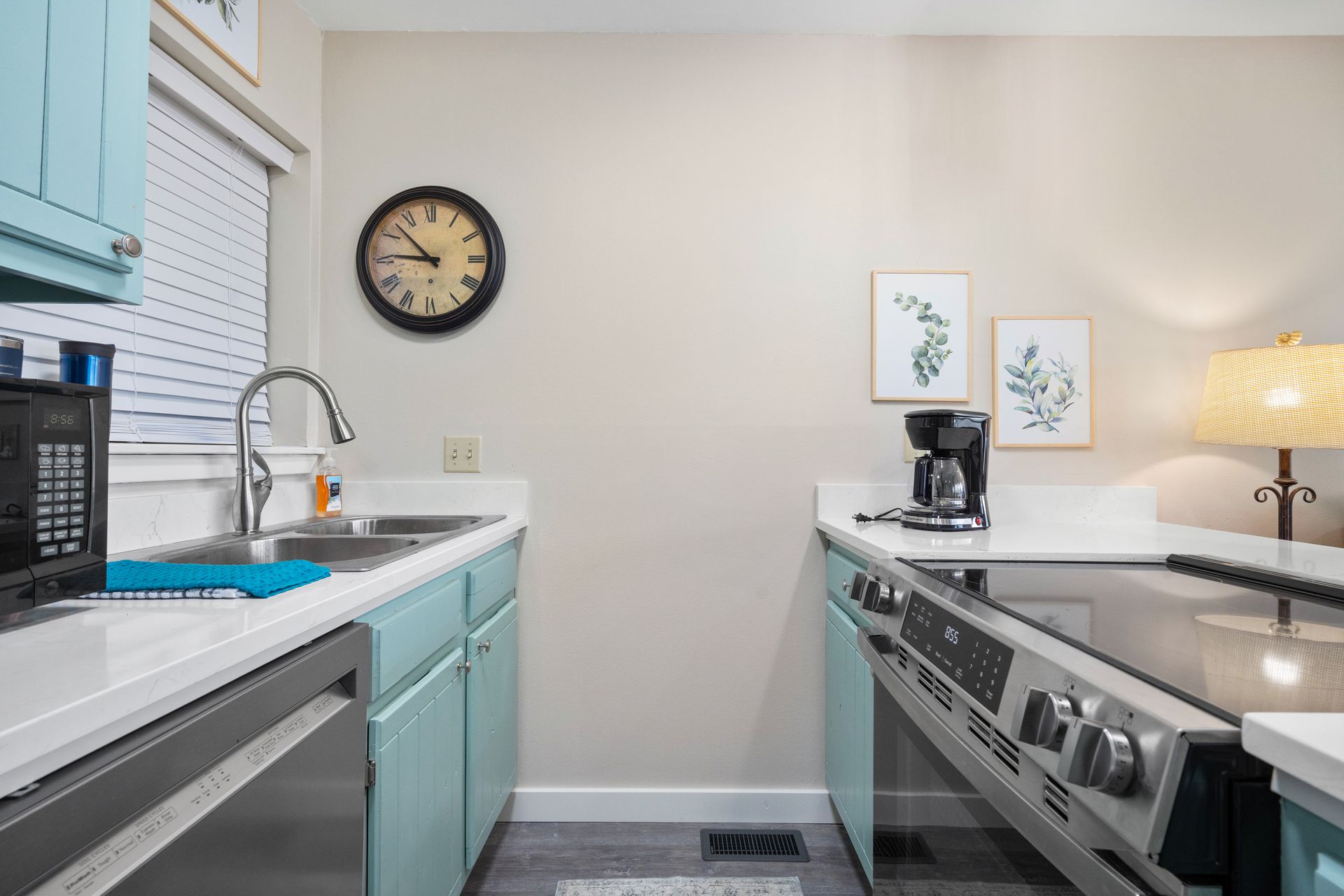 A kitchen with blue cabinets , a stove , a sink , and a clock on the wall.