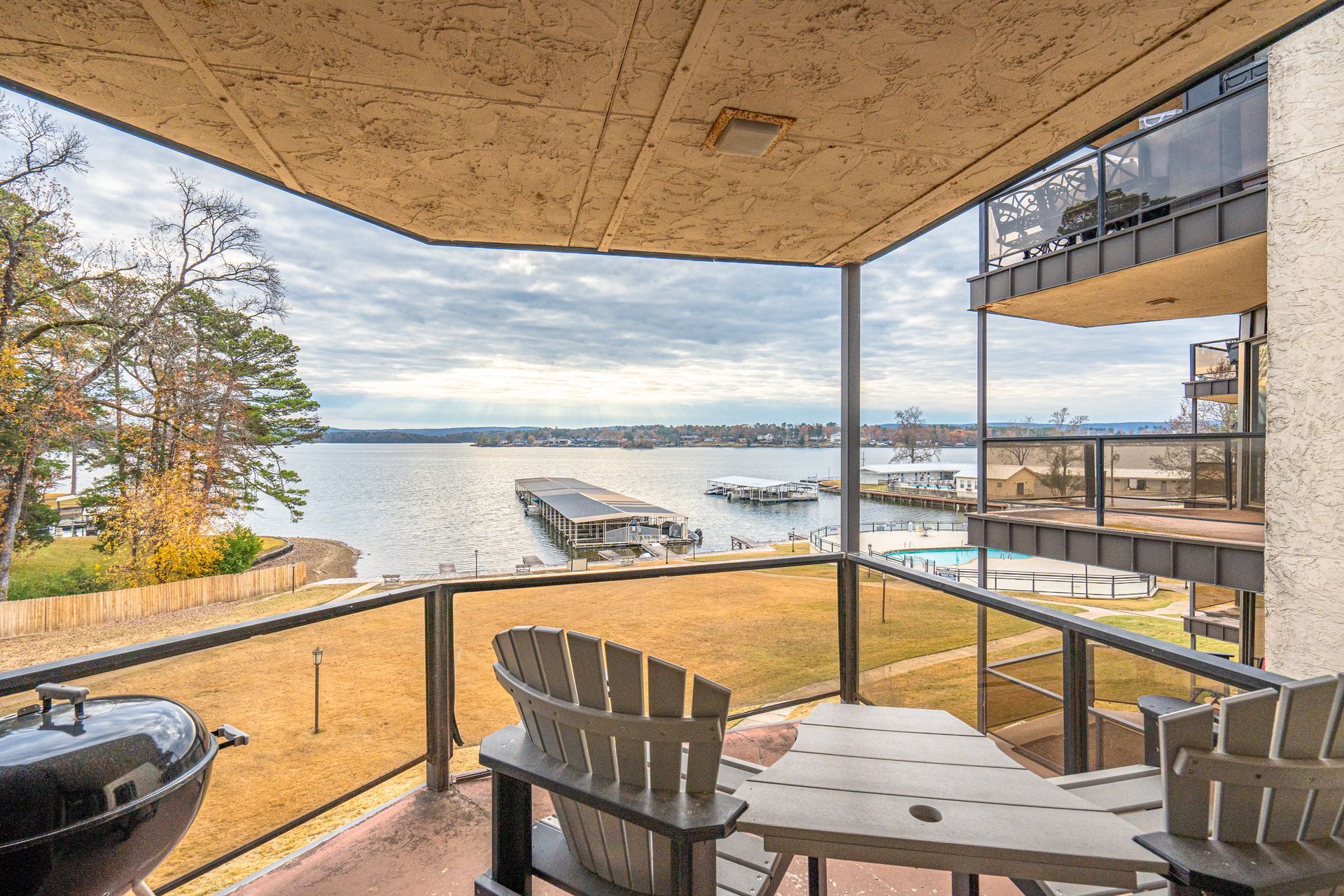 A balcony with chairs , a table and a grill overlooking a lake.