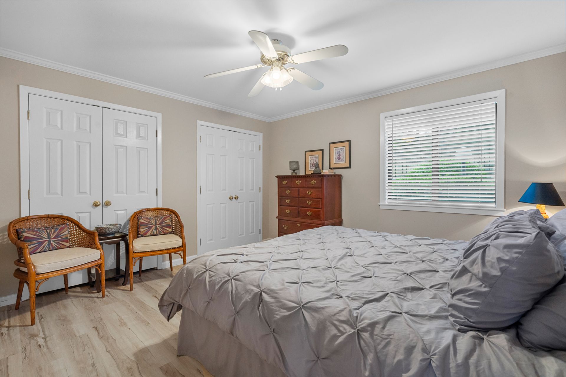 A bedroom with a bed , dresser , chairs and a ceiling fan.