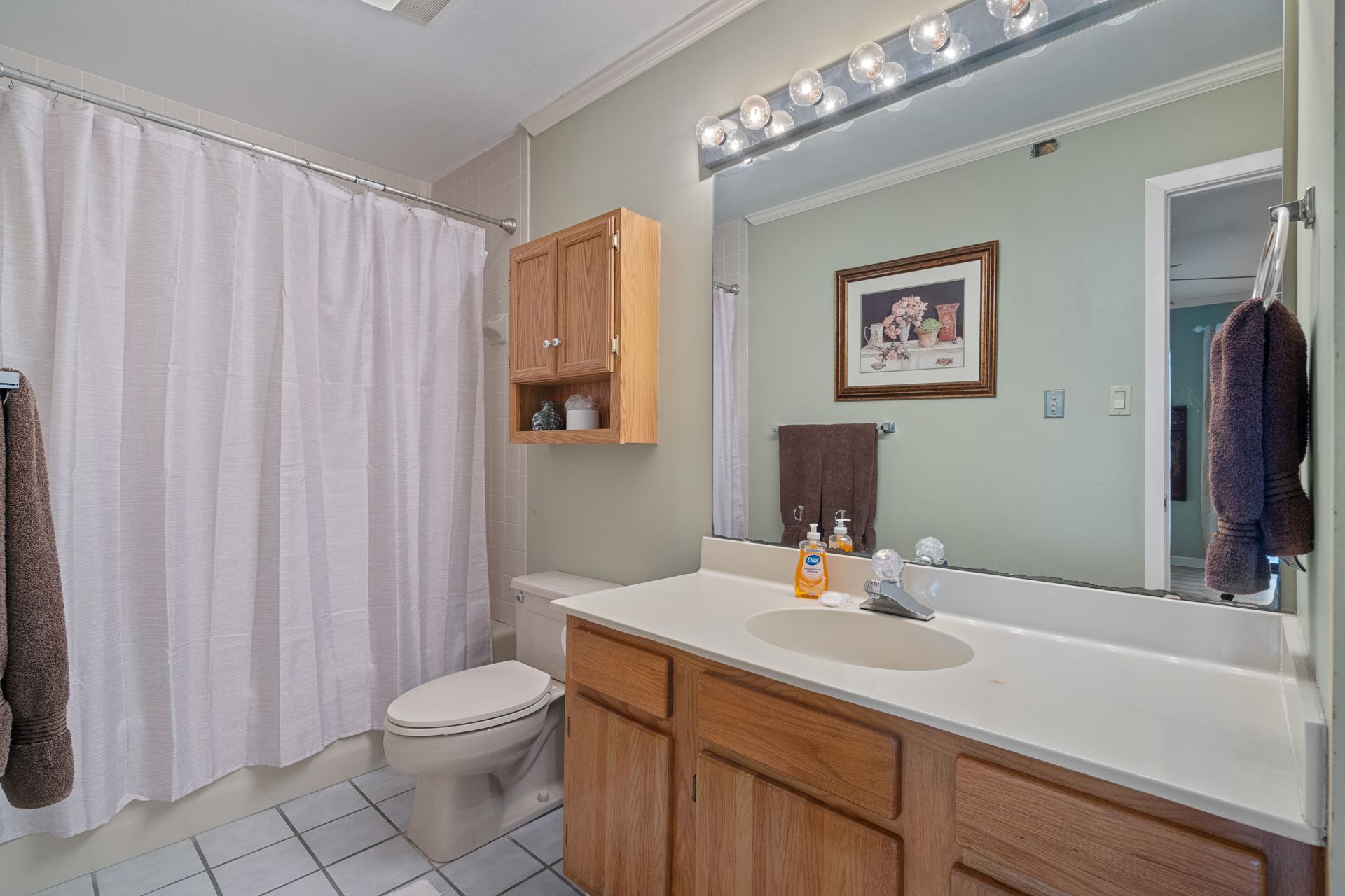 A bathroom with a toilet , sink , mirror and shower curtain.