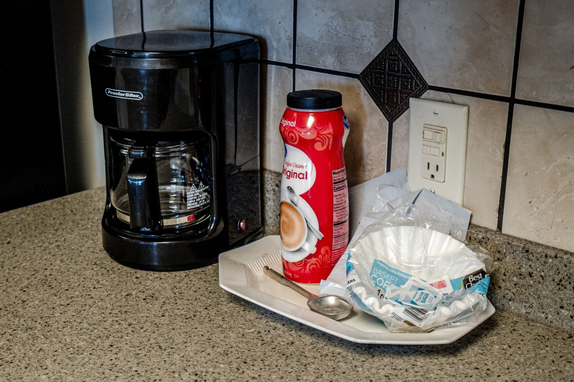 A coffee maker is sitting on a counter next to a can of soda.