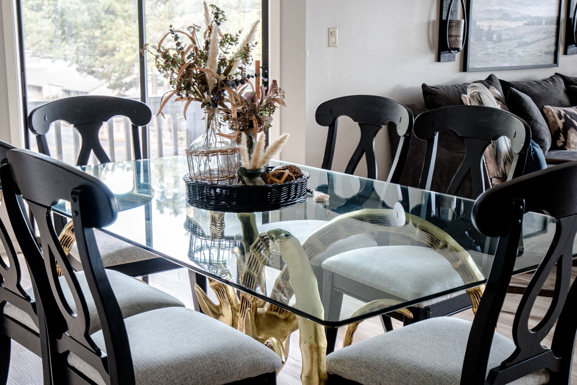 A dining room with a glass table and chairs and a vase of flowers on it.