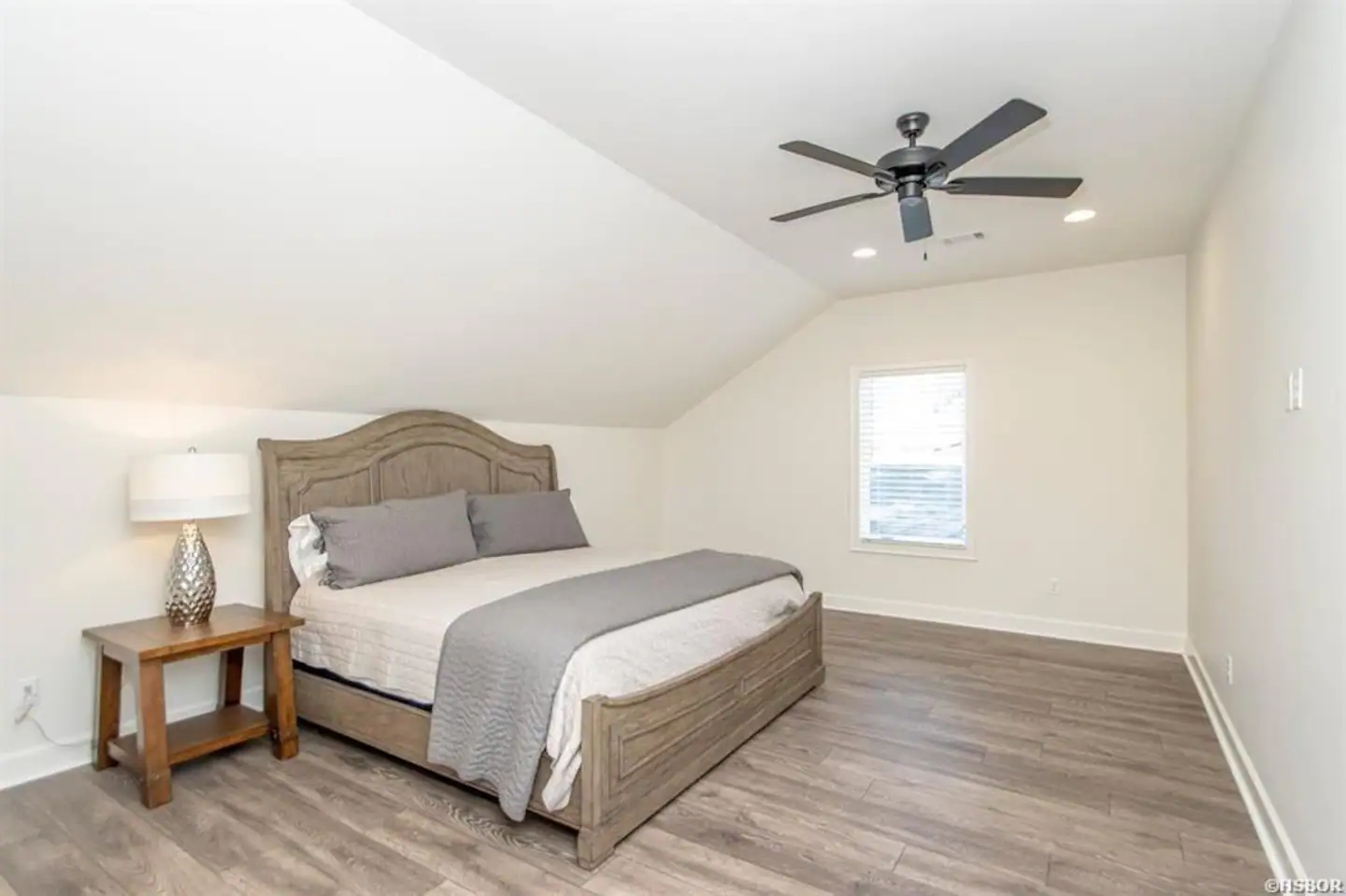 A bedroom with a bed , nightstand , lamp and ceiling fan.