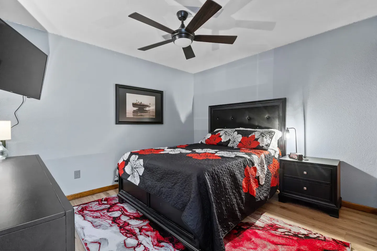 A bedroom with a bed , nightstand , rug and ceiling fan.