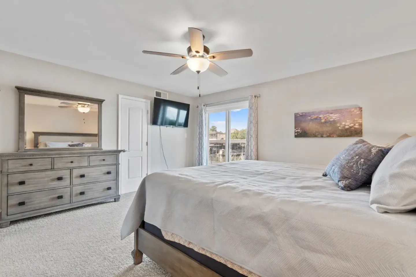 A bedroom with a king size bed , dresser , mirror and ceiling fan.