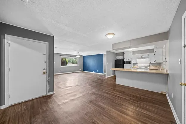 An empty living room with hardwood floors and a kitchen.