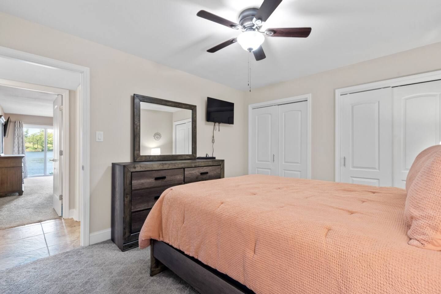 A bedroom with a king size bed , dresser , mirror and ceiling fan.