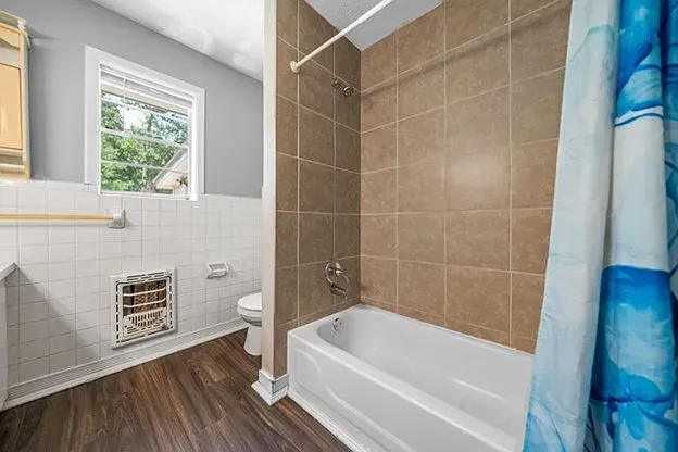 A bathroom with a tub , toilet , window and shower curtain.