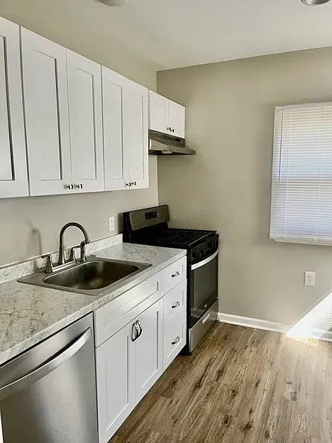 A kitchen with white cabinets , stainless steel appliances , a sink , and a window.