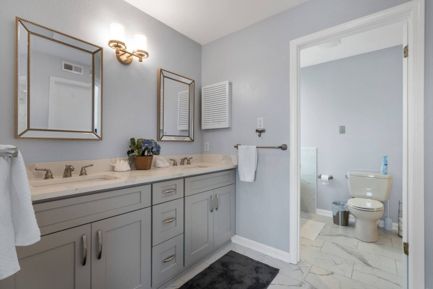 A bathroom with two sinks , two mirrors and a toilet.