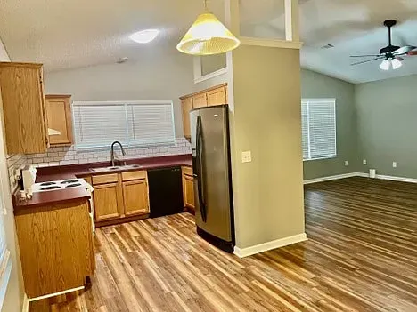 A kitchen with stainless steel appliances , wooden cabinets , hardwood floors and a ceiling fan.