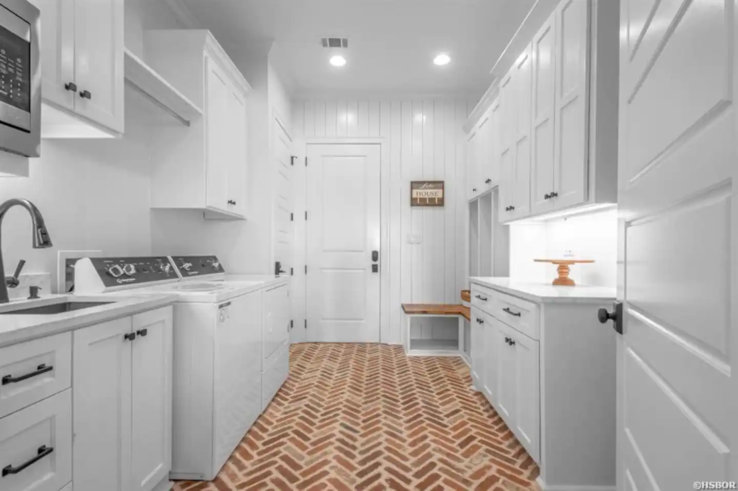 A laundry room with white cabinets and a brick floor.