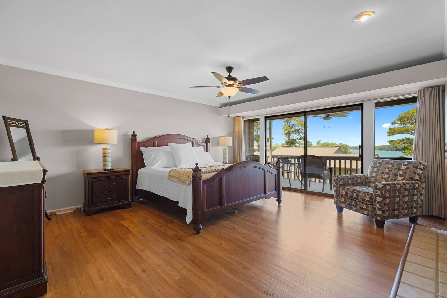 A bedroom with hardwood floors , a large bed , a chair , a dresser and a ceiling fan.