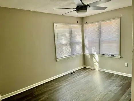 An empty room with a ceiling fan and two windows.