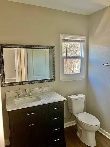 A bathroom with a sink , toilet , mirror and window.