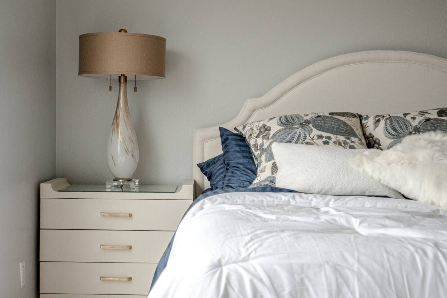 A bedroom with a bed , nightstand , lamp and dresser.
