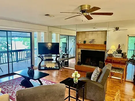 Living room with fireplace, deck access, TV, black tables, and a ceiling fan.