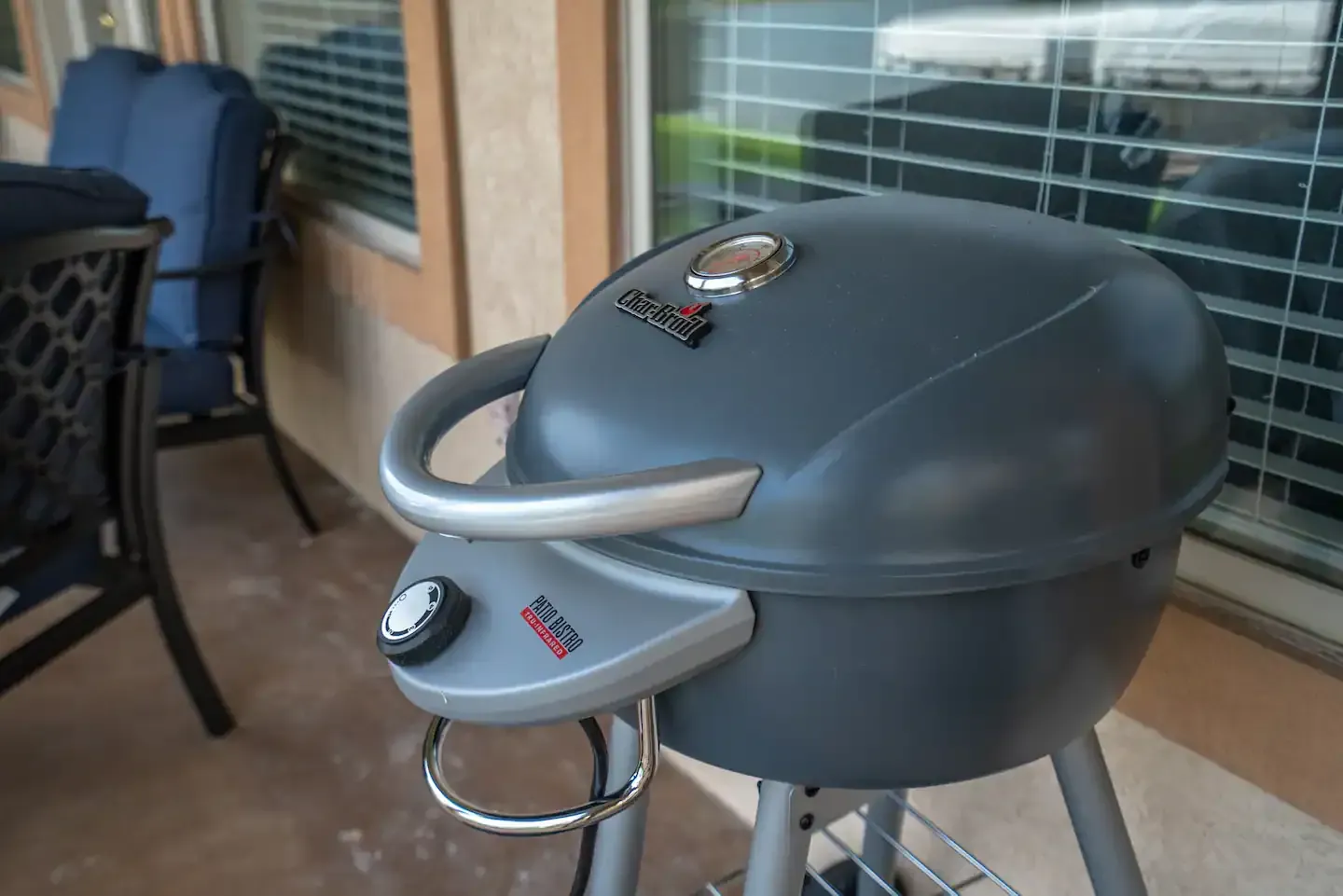 A grill is sitting on a patio next to a window.