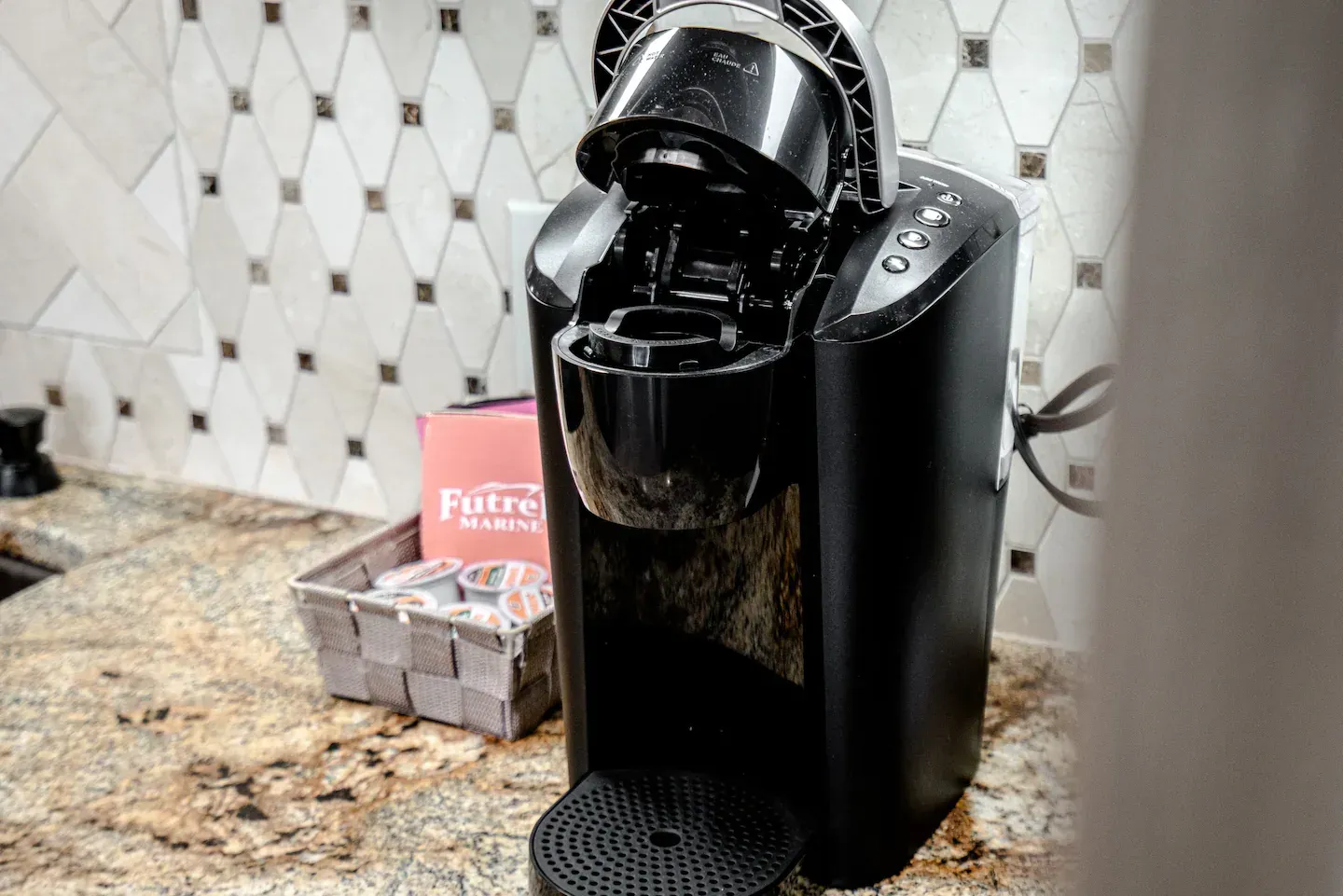 A black coffee maker is sitting on a granite counter.