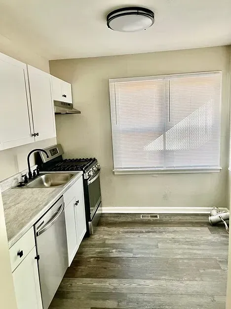 A kitchen with a stove , sink , dishwasher and window.