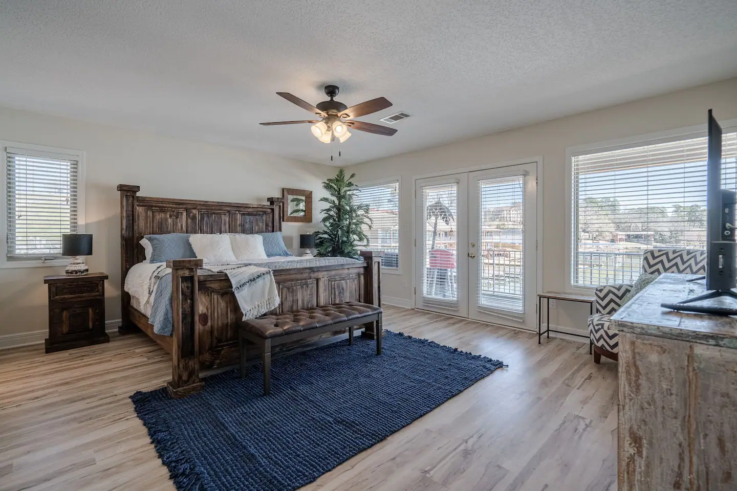 A large bedroom with a king size bed , a rug , a ceiling fan , and a flat screen tv.