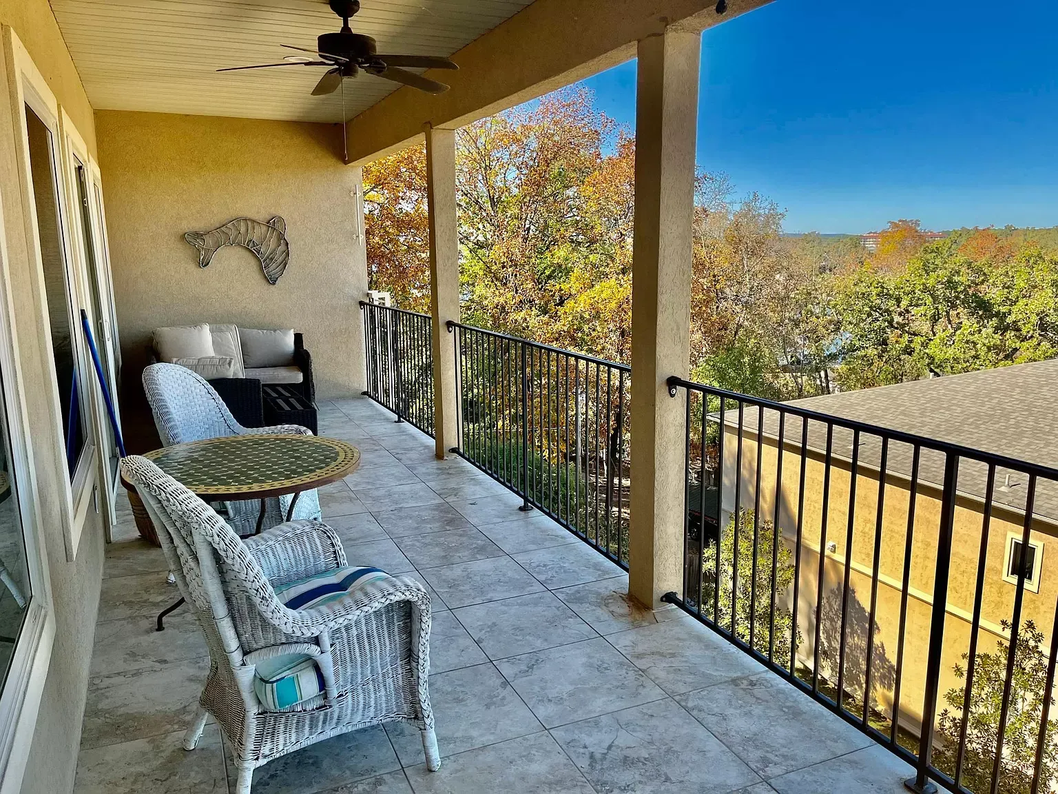 A balcony with wicker chairs , a table and a ceiling fan.