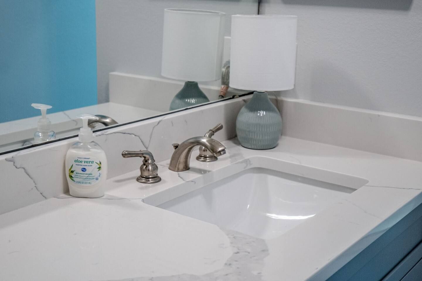 A bathroom with a sink , mirror , lamp and soap dispenser.
