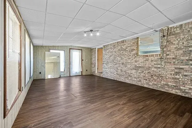 An empty room with hardwood floors and a brick wall.
