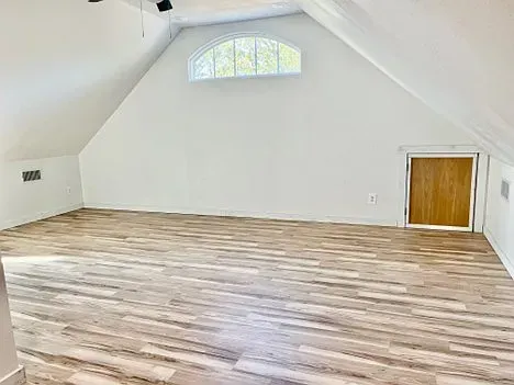 An empty attic with hardwood floors and a window.