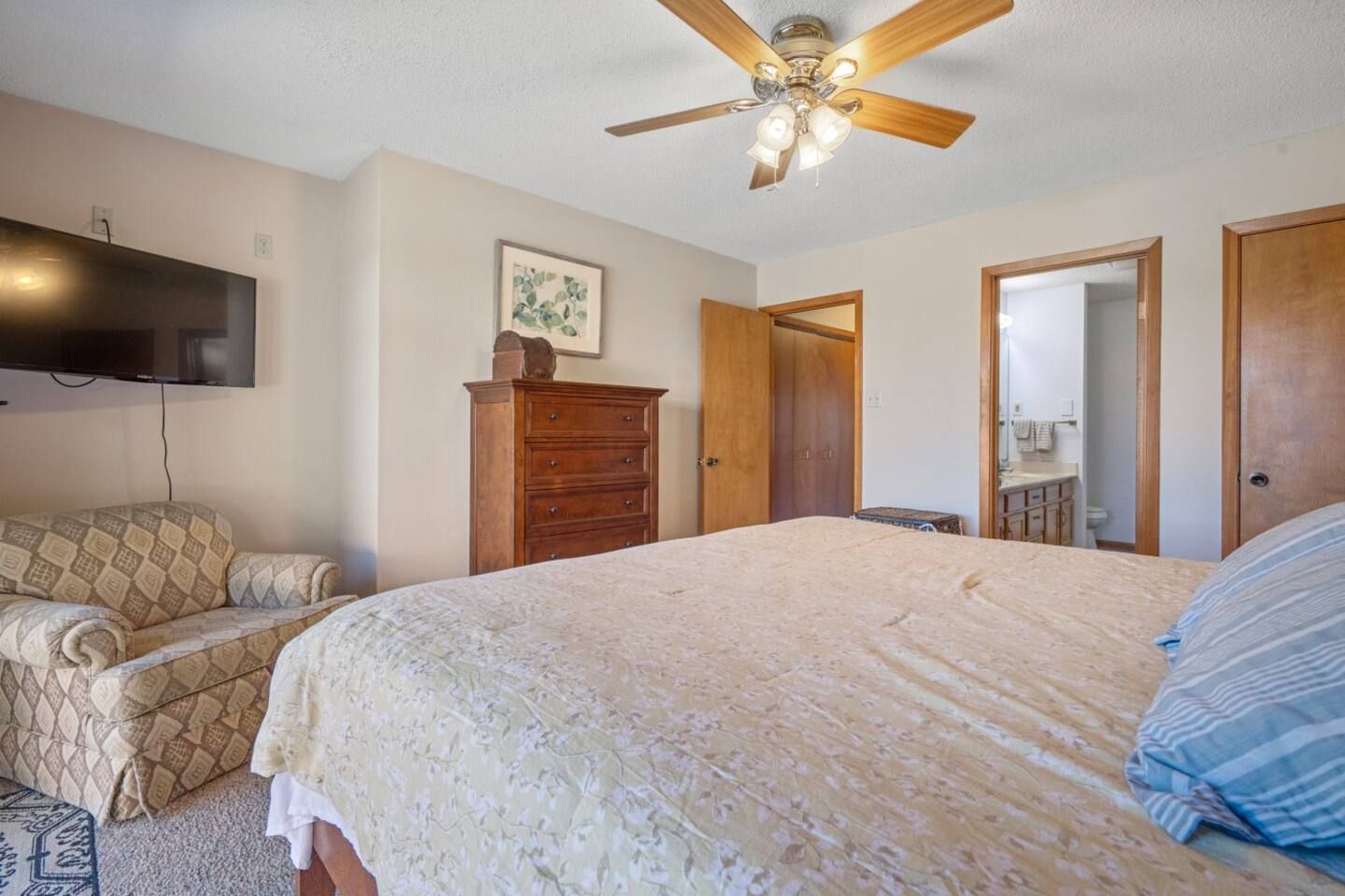 A bedroom with a bed , dresser , chair , television and ceiling fan.