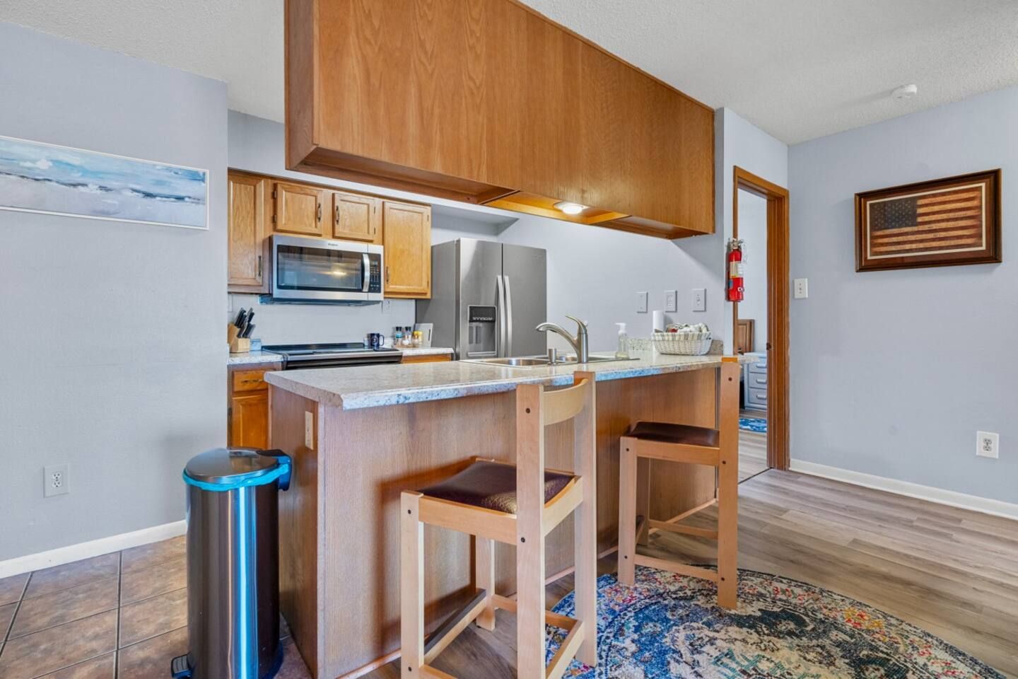 A kitchen with a large island , stools , a refrigerator and a microwave.