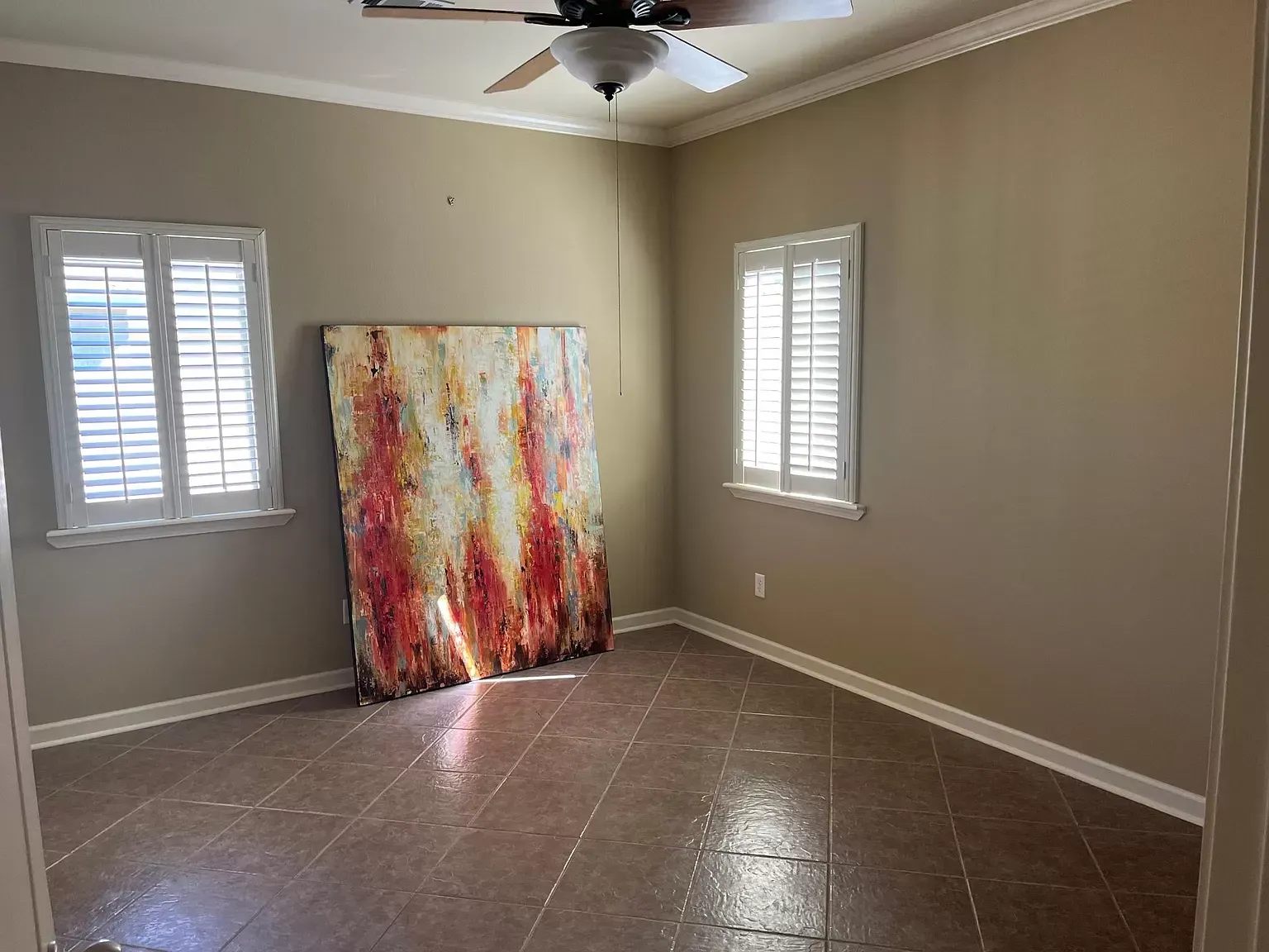 An empty room with a painting on the wall and a ceiling fan.